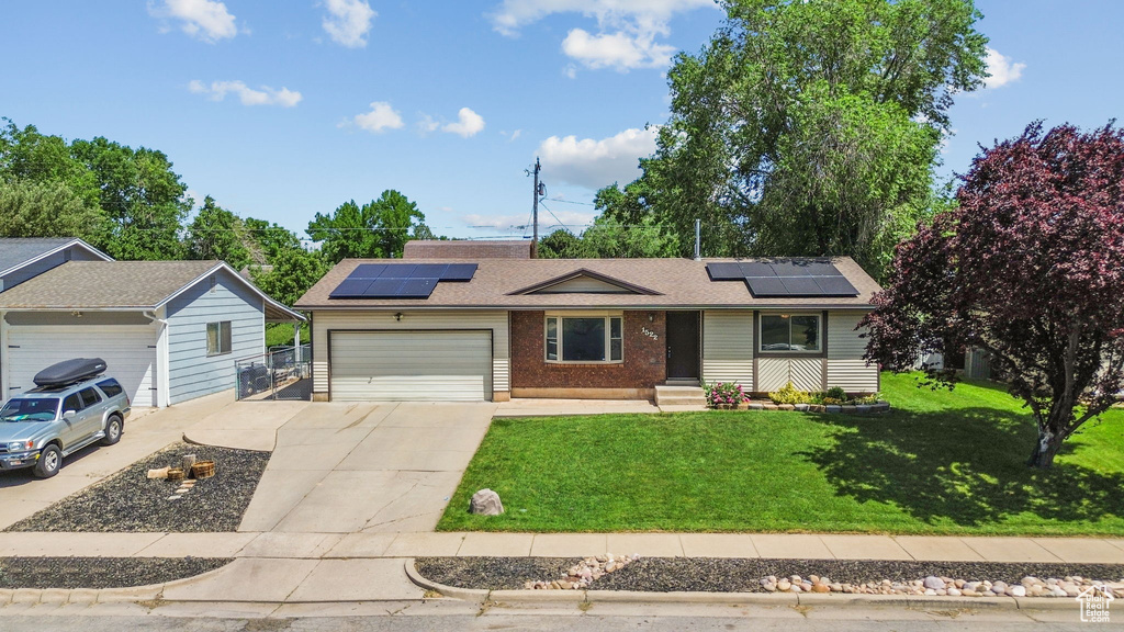 Single story home with concrete driveway, an attached garage, a front lawn, and roof mounted solar panels