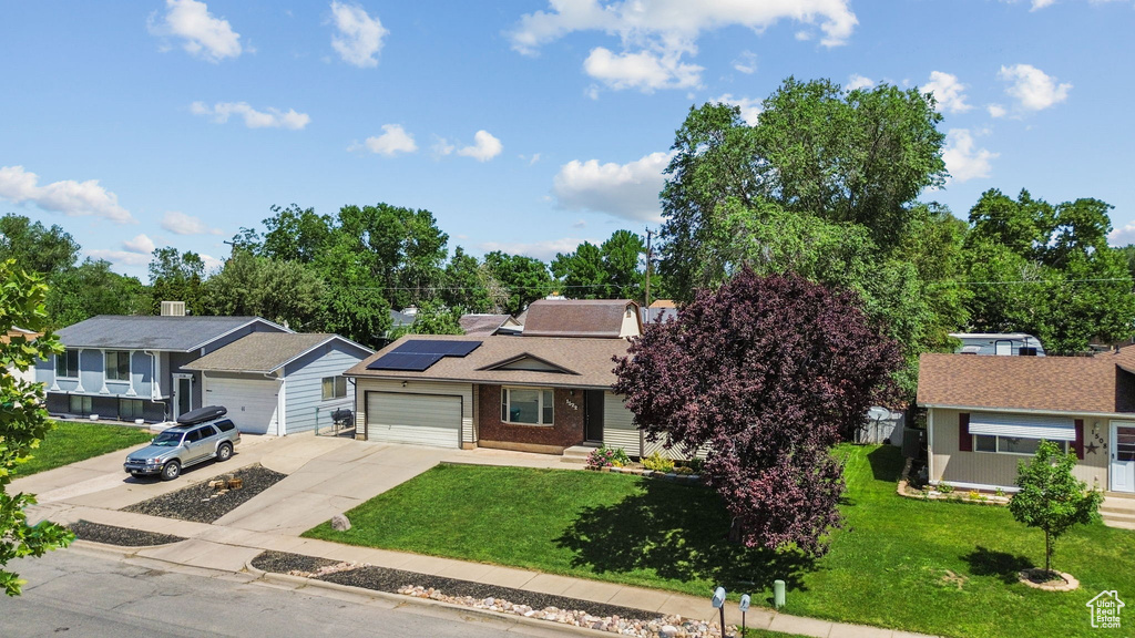 View of front of property featuring driveway, a front yard, solar panels, and a garage