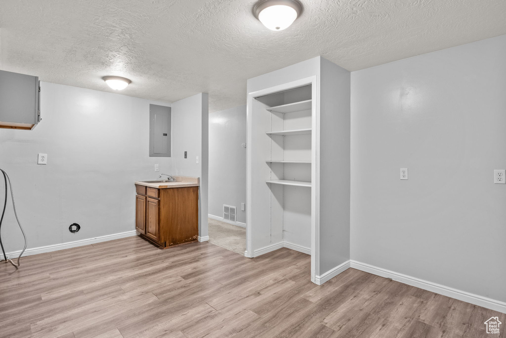 Bar area with a textured ceiling, light wood finished floors, electric panel, and baseboards