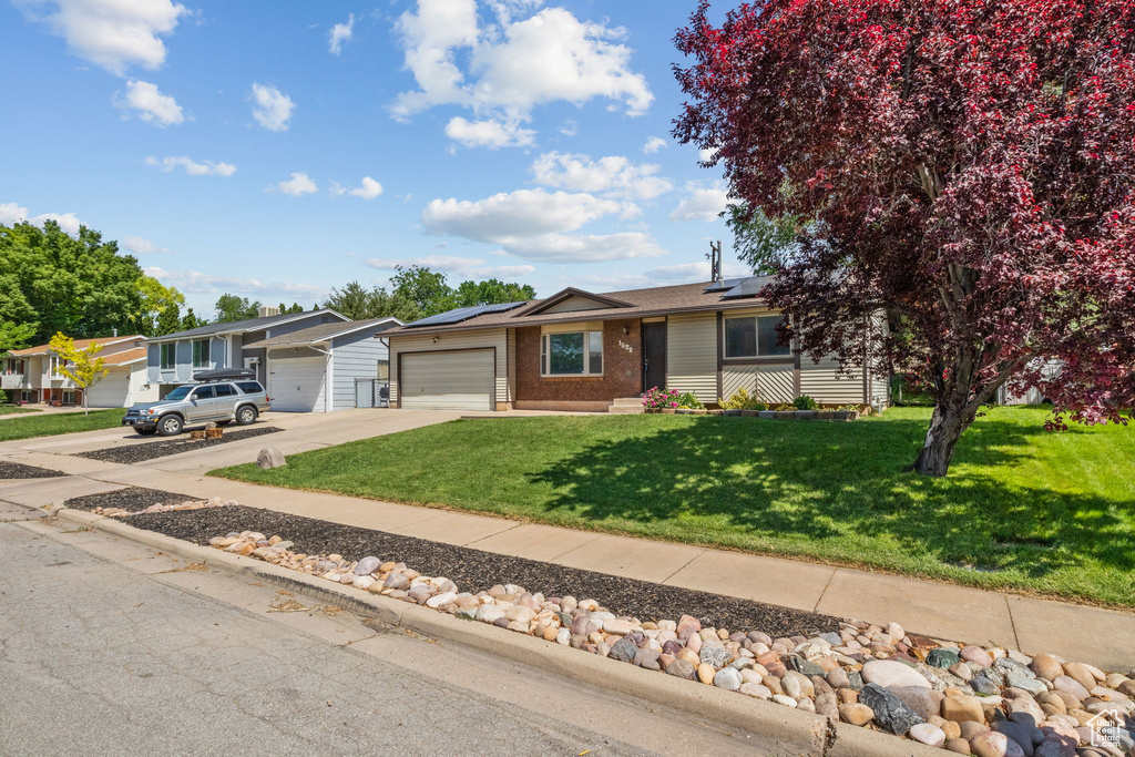 View of front of home with brick siding, a garage, driveway, a front lawn, and roof mounted solar panels