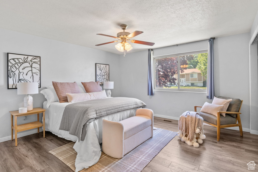 Bedroom with wood finished floors, baseboards, a textured ceiling, and a ceiling fan