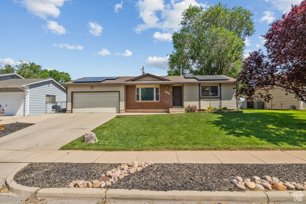 Ranch-style home with an attached garage, concrete driveway, a front lawn, roof mounted solar panels, and brick siding
