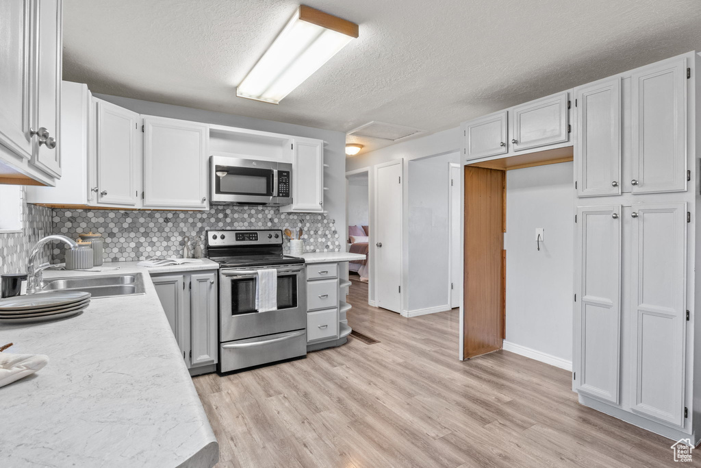 Kitchen with appliances with stainless steel finishes, a sink, light countertops, a textured ceiling, and tasteful backsplash