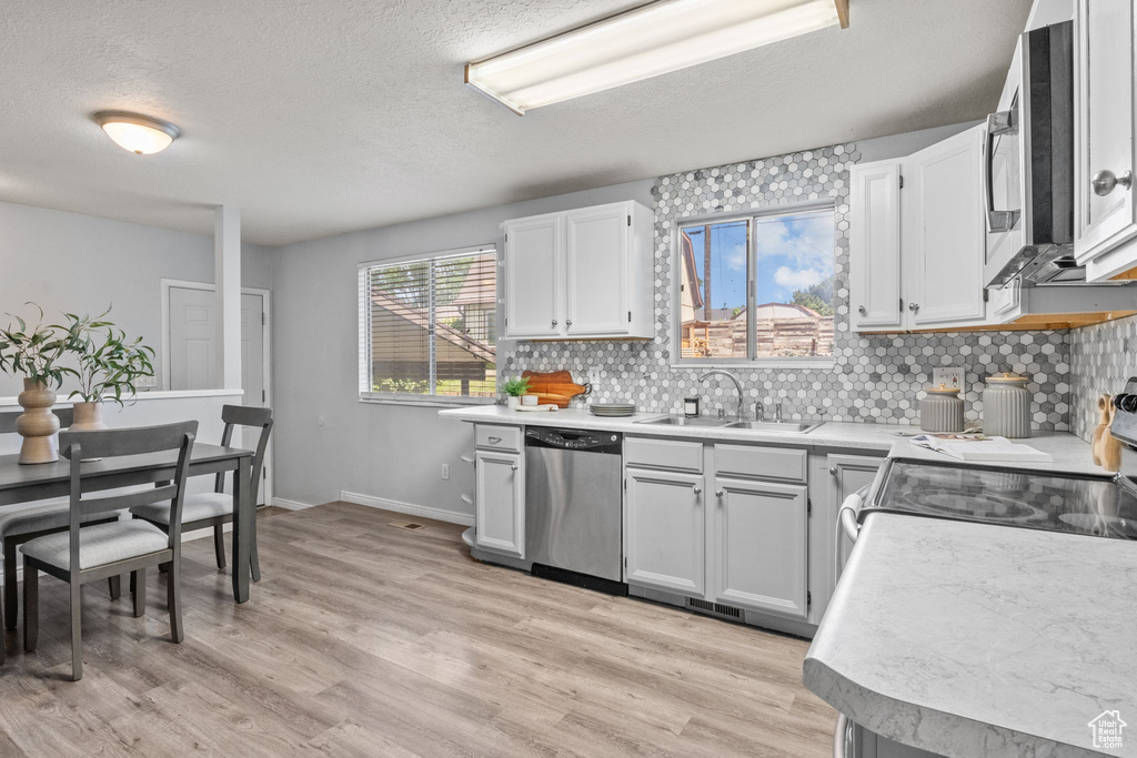Kitchen with dishwasher, a sink, electric stove, a textured ceiling, and light wood-type flooring
