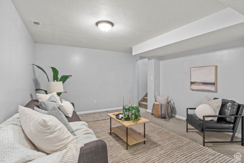 Living room with stairway, light colored carpet, a textured ceiling, and baseboards