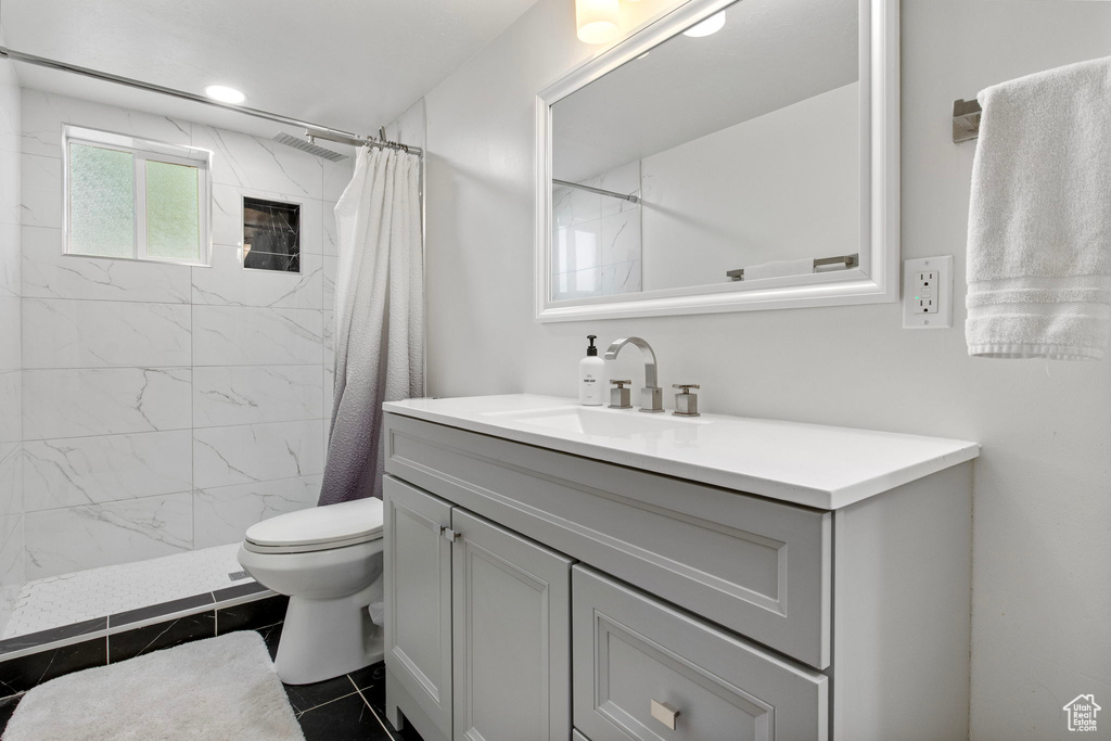 Bathroom featuring vanity, toilet, tiled shower, and tile patterned floors