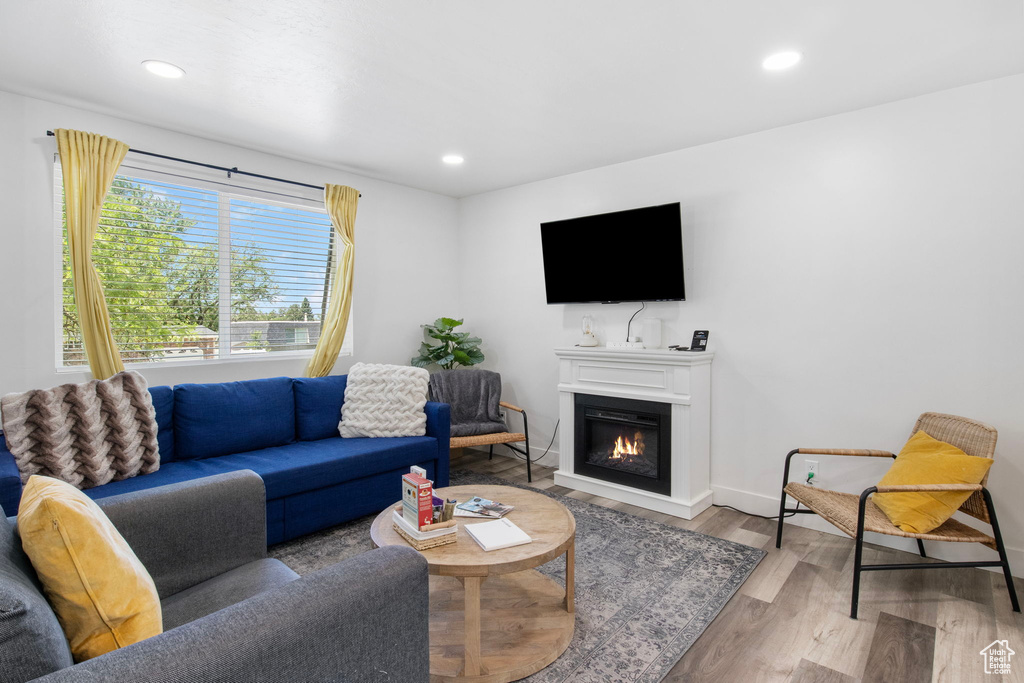Living room with wood finished floors, a glass covered fireplace, baseboards, and recessed lighting