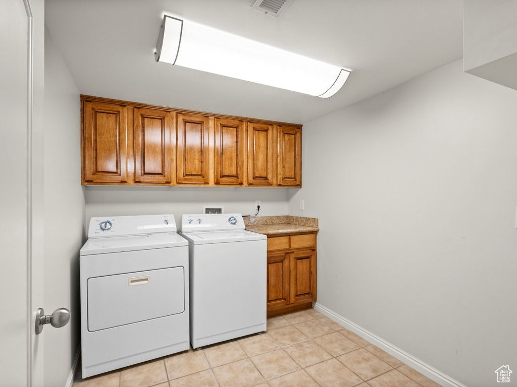 Laundry area with cabinet space, independent washer and dryer, light tile patterned floors, and baseboards