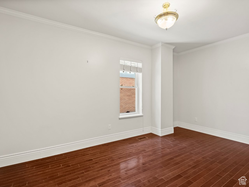 Spare room featuring dark wood-style floors, ornamental molding, and baseboards