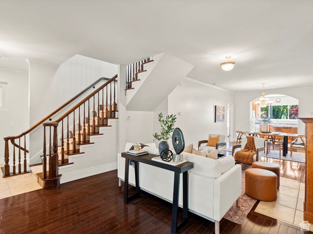 Living room with wood finished floors, stairs, baseboards, a chandelier, and crown molding