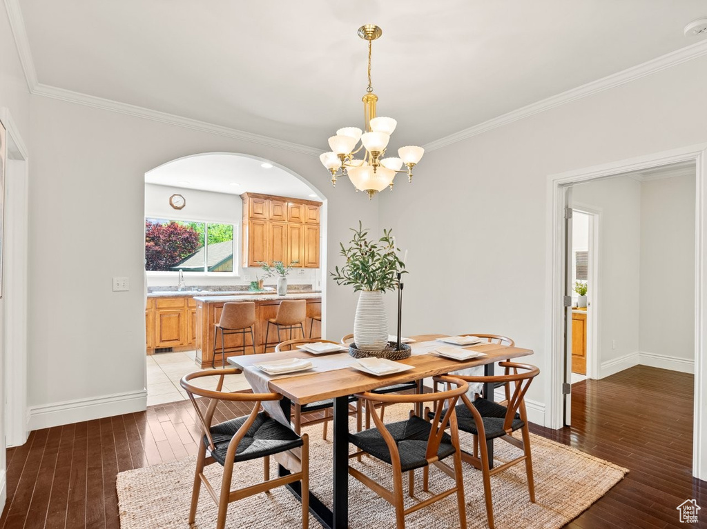Dining area with hardwood / wood-style floors, a chandelier, baseboards, and crown molding