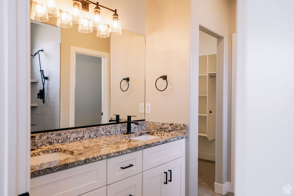 Full bathroom with double vanity, a chandelier, a spacious closet, tiled shower, and baseboards