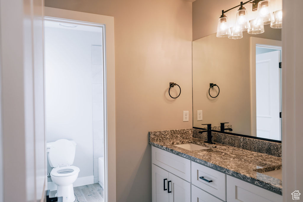 Bathroom featuring vanity, toilet, a chandelier, wood finished floors, and baseboards