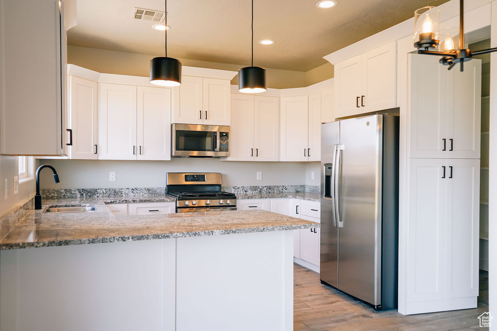 Kitchen with stainless steel appliances, a sink, a peninsula, light stone countertops, and recessed lighting