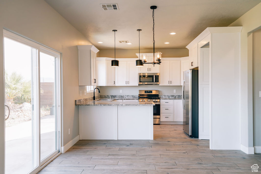 Kitchen featuring stainless steel appliances, a peninsula, a sink, light stone countertops, and light wood-type flooring