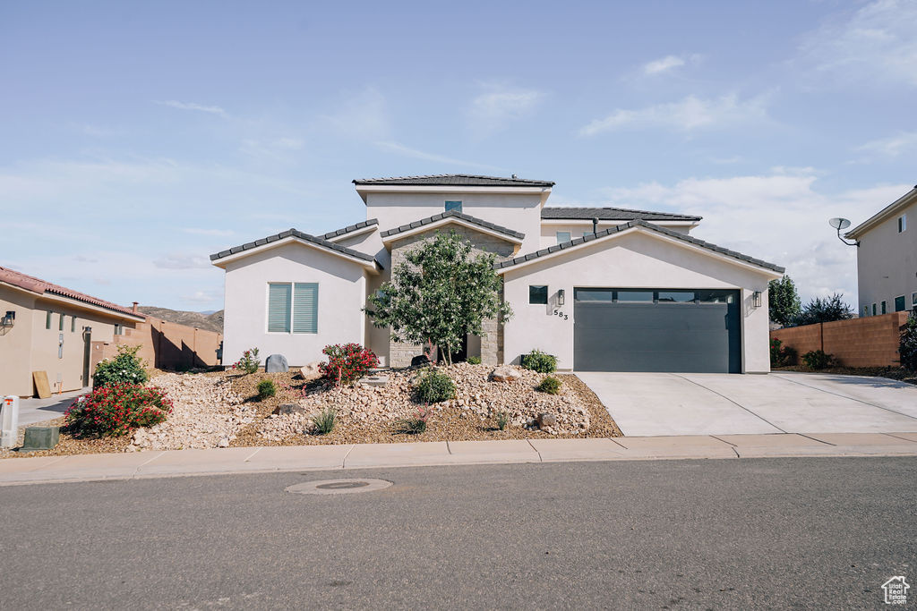 View of front of home with an attached garage, stucco siding, concrete driveway, and a tiled roof