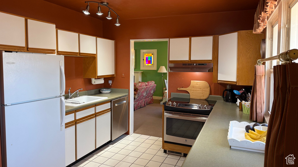 Kitchen with appliances with stainless steel finishes, under cabinet range hood, a sink, light countertops, and white cabinetry