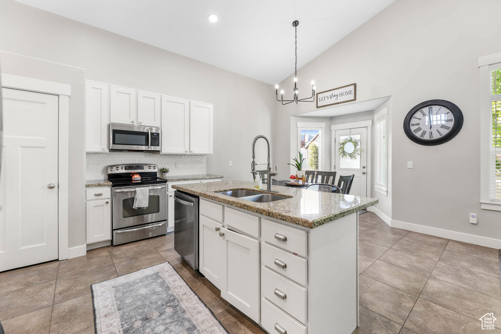 Kitchen featuring stainless steel appliances, a sink, white cabinets, tasteful backsplash, and light stone counters