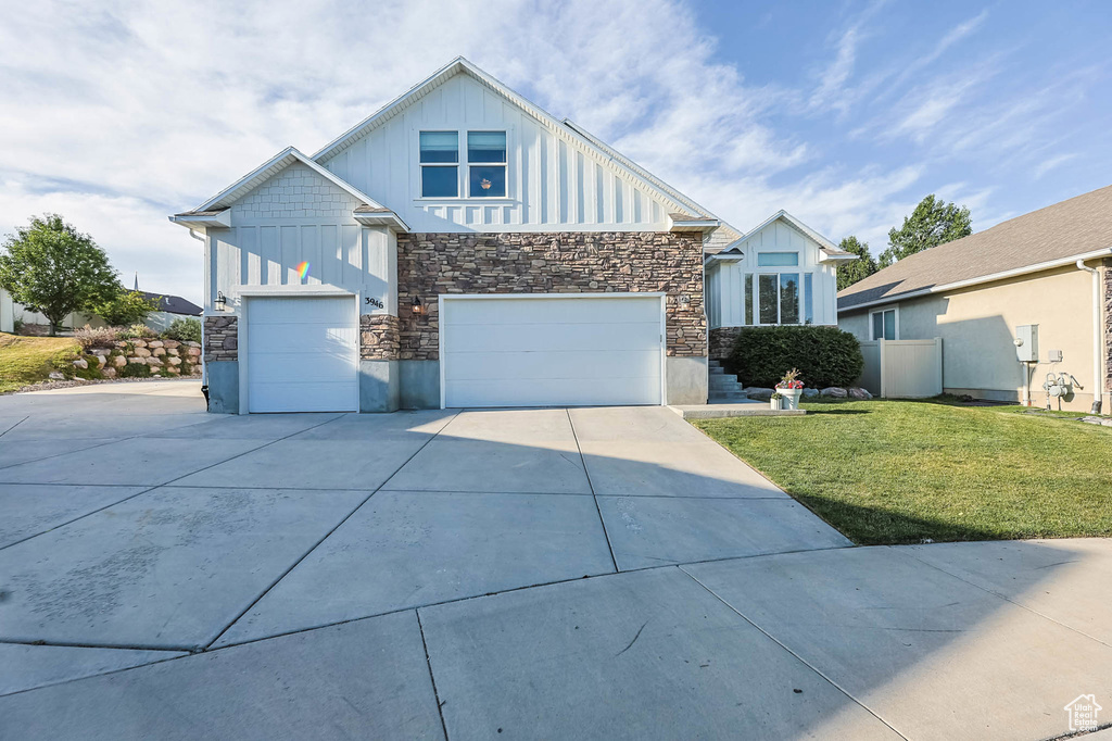 View of front of house with board and batten siding, concrete driveway, stone siding, a front yard, and an attached garage