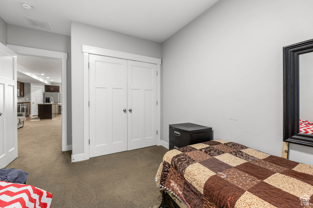 Carpeted bedroom featuring stainless steel fridge, a closet, and baseboards