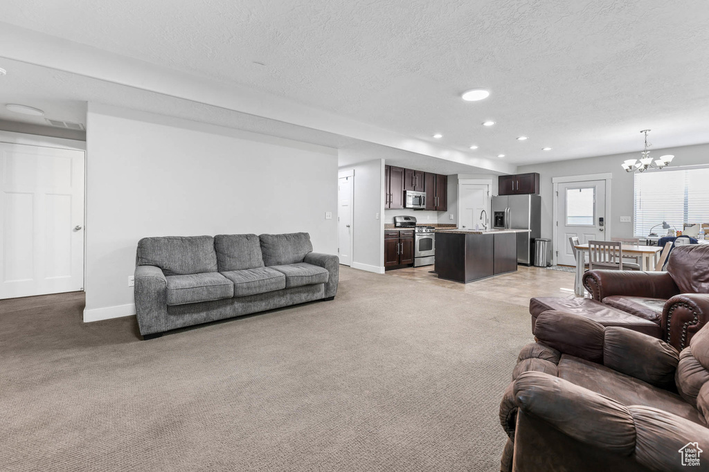 Living room featuring a chandelier, a textured ceiling, light carpet, baseboards, and recessed lighting