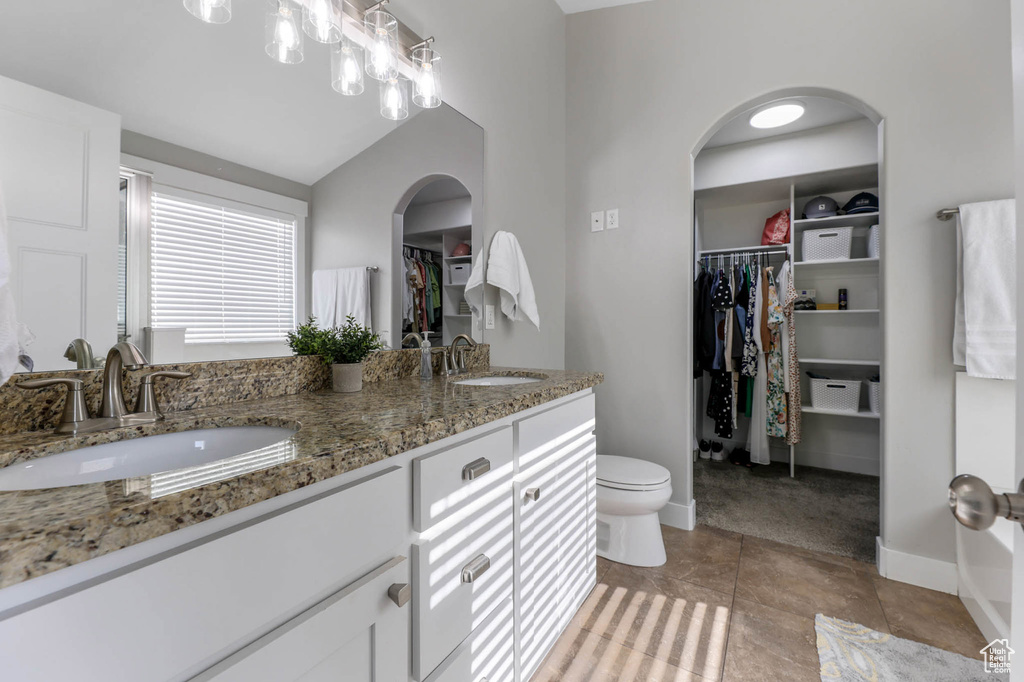 Bathroom with double vanity, a walk in closet, toilet, baseboards, and vaulted ceiling