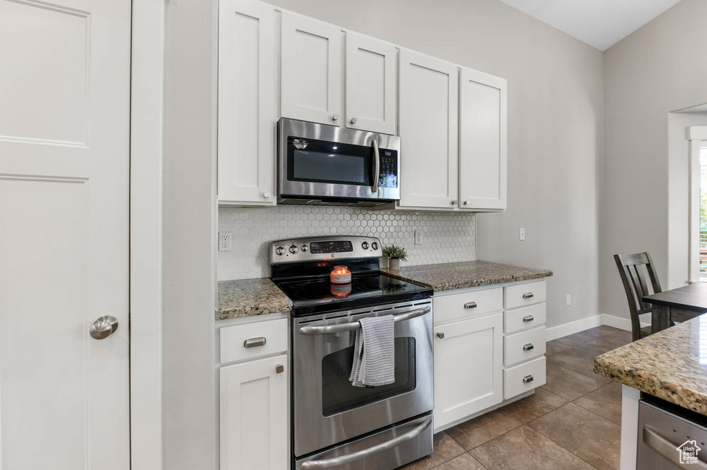 Kitchen featuring appliances with stainless steel finishes, decorative backsplash, light stone counters, and white cabinets