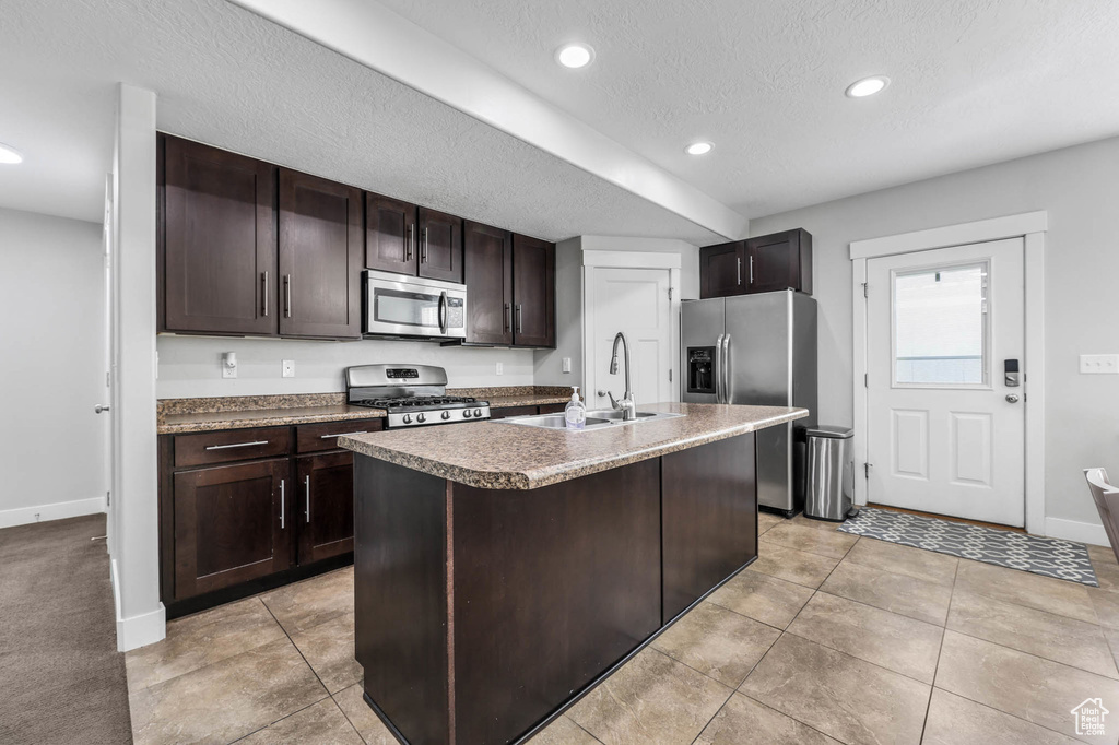 Kitchen with appliances with stainless steel finishes, a sink, baseboards, dark brown cabinets, and recessed lighting