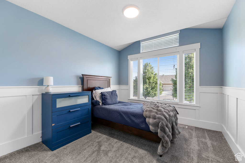 Bedroom with wainscoting, carpet, a decorative wall, and lofted ceiling