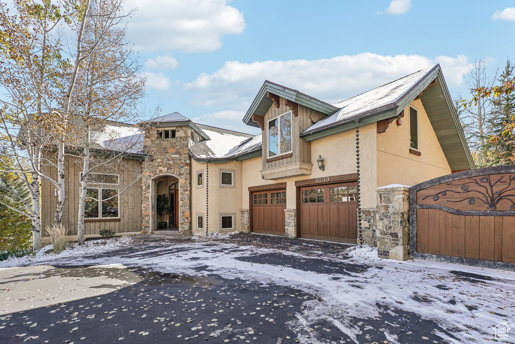 View of front facade with stone siding, driveway, stucco siding, and a gate