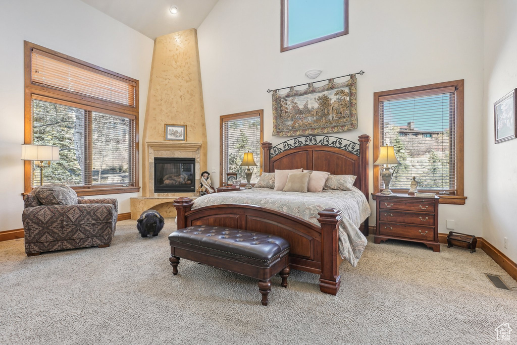 Carpeted bedroom with a towering ceiling, baseboards, multiple windows, and a premium fireplace