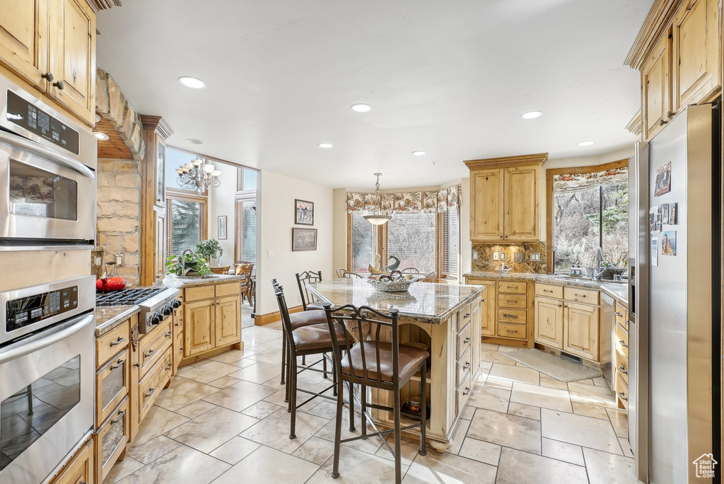 Kitchen with stainless steel appliances, a kitchen island, recessed lighting, a breakfast bar, and light stone countertops