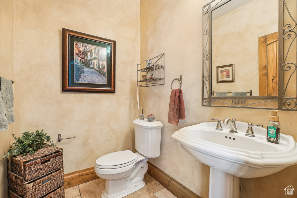 Bathroom with toilet, baseboards, tile patterned floors, and a sink