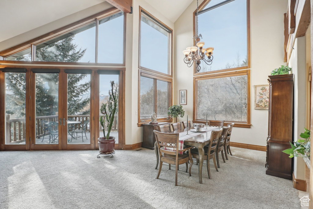 Carpeted dining area with high vaulted ceiling, baseboards, and a chandelier