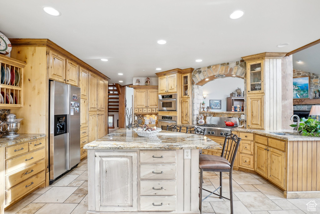 Kitchen with stainless steel fridge, a kitchen island, recessed lighting, glass insert cabinets, and a breakfast bar