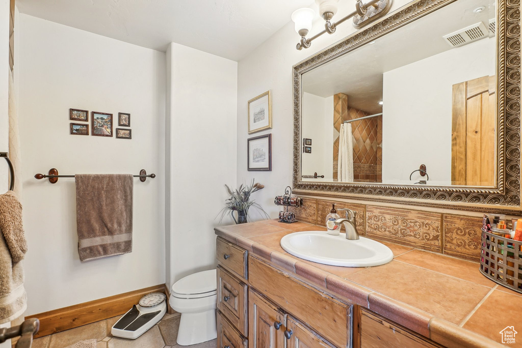 Bathroom with vanity, toilet, curtained shower, tile patterned flooring, and baseboards