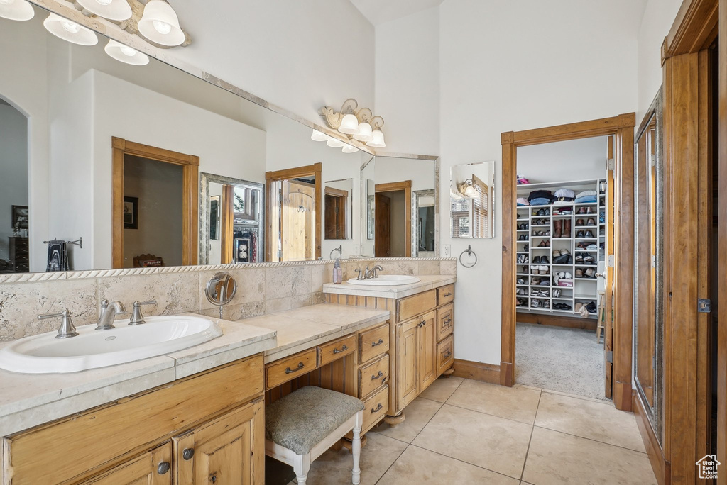 Bathroom featuring double vanity, a spacious closet, tile patterned flooring, and tasteful backsplash