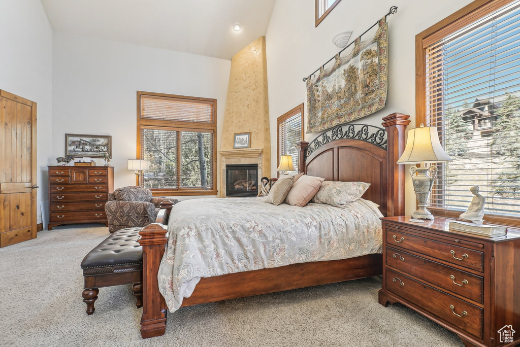 Bedroom featuring light carpet, a high ceiling, and a fireplace