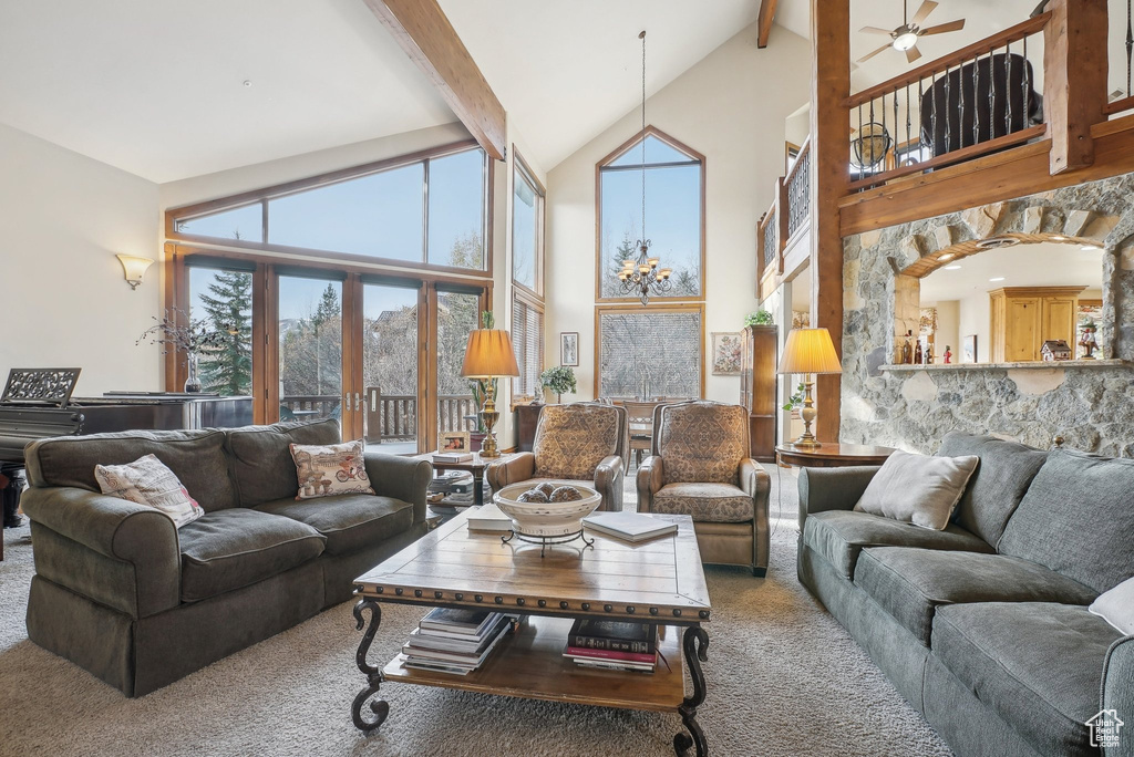Carpeted living area featuring high vaulted ceiling, beamed ceiling, a ceiling fan, and a chandelier