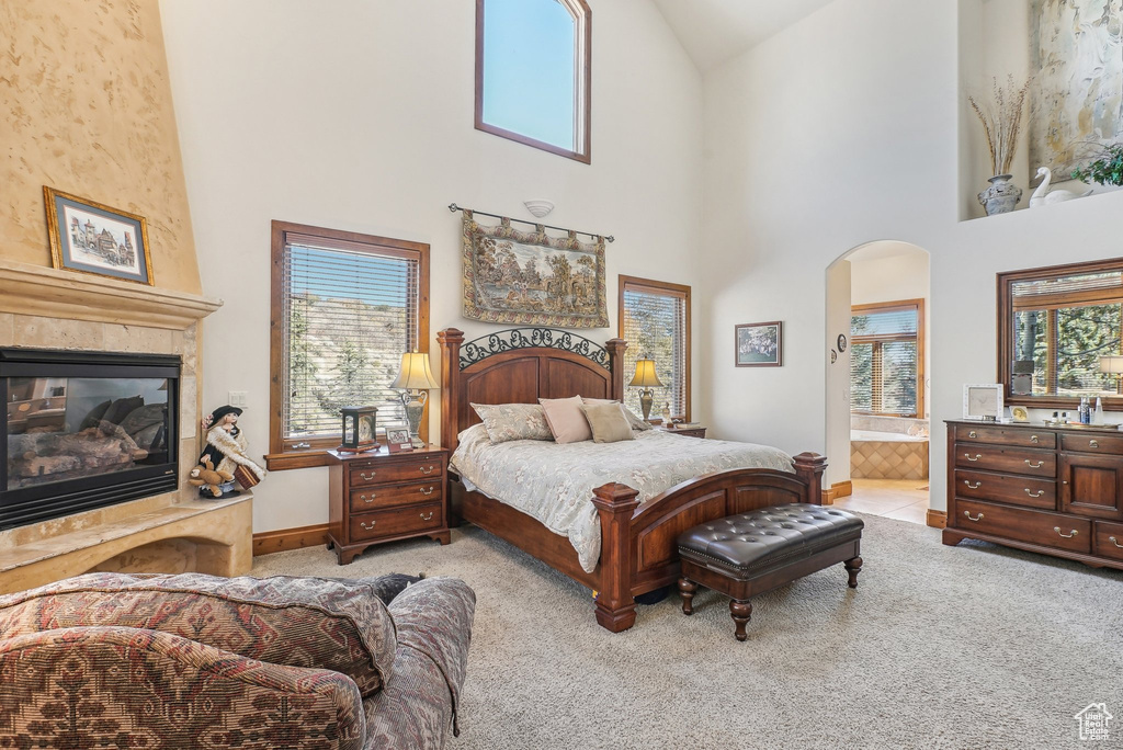 Bedroom with carpet floors, arched walkways, a fireplace, high vaulted ceiling, and ensuite bath