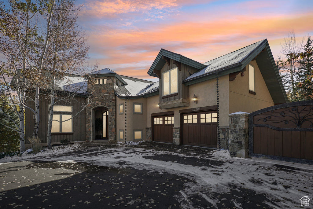 View of front of house featuring stone siding, driveway, stucco siding, and a gate