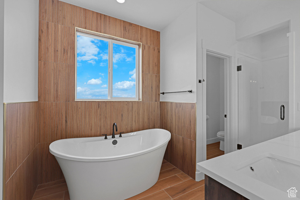 Full bath featuring a soaking tub, vanity, wainscoting, toilet, and wood finished floors