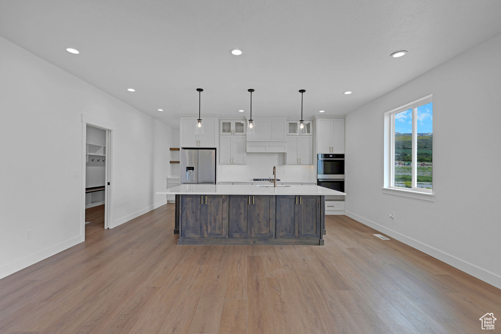 Kitchen featuring appliances with stainless steel finishes, white cabinets, light countertops, a large island, and recessed lighting