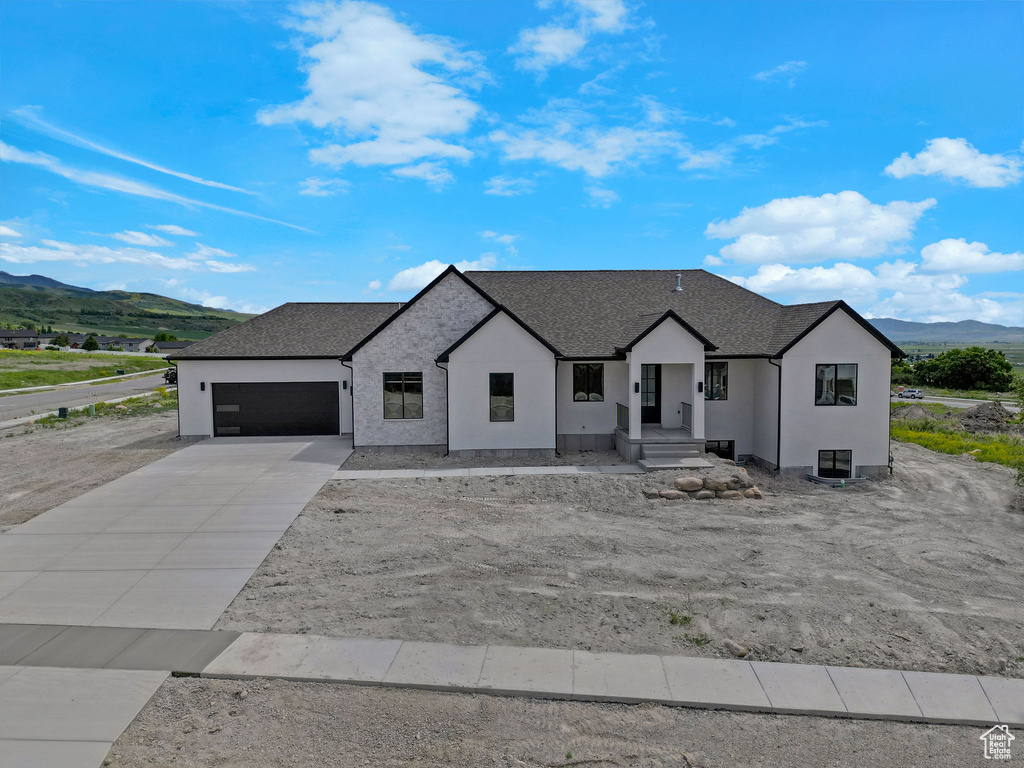 Modern farmhouse featuring a mountain view, a garage, concrete driveway, stucco siding, and roof with shingles