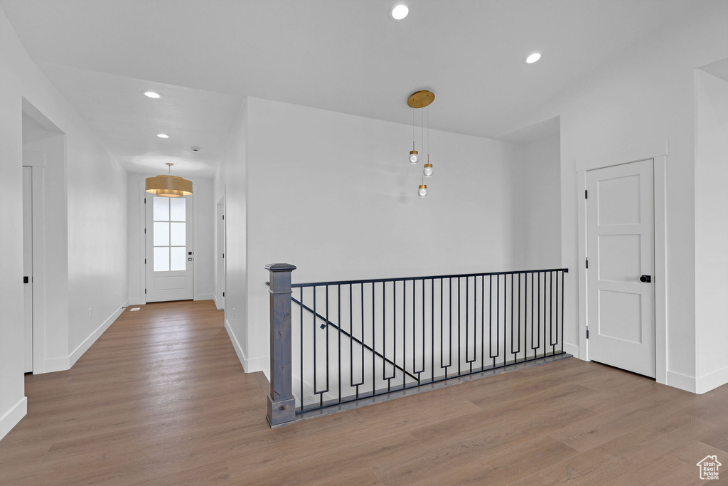 Hallway with wood finished floors, baseboards, recessed lighting, and an upstairs landing