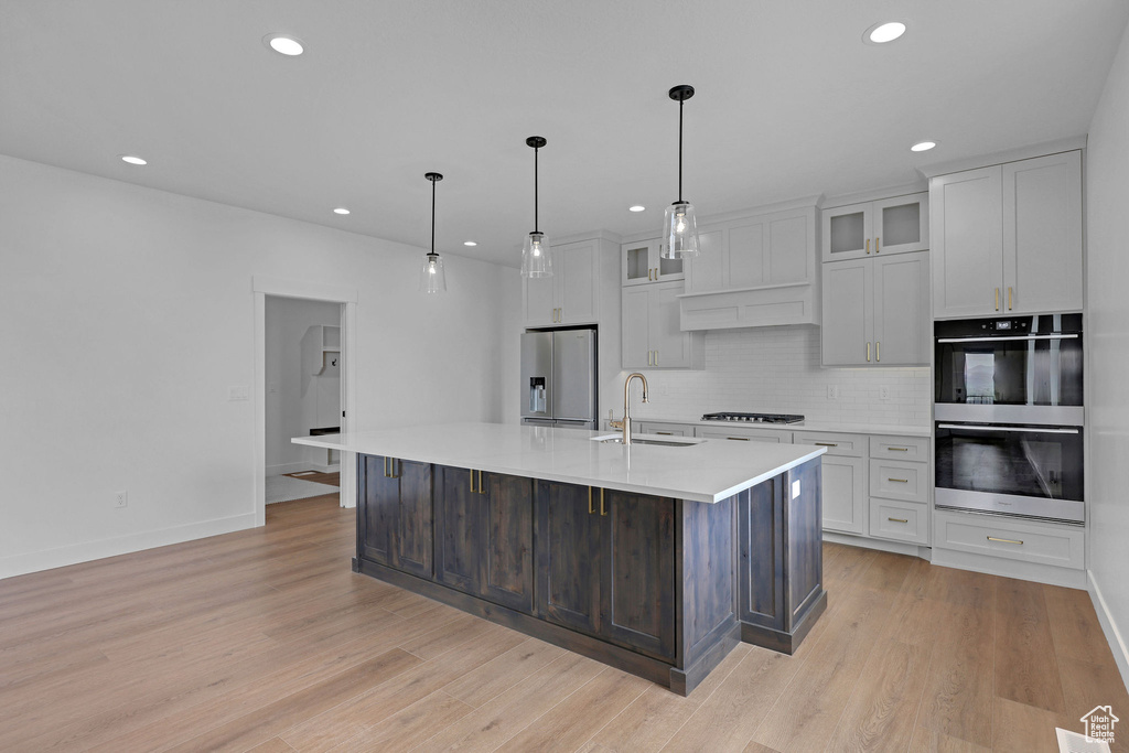 Kitchen featuring appliances with stainless steel finishes, a sink, recessed lighting, decorative backsplash, and light countertops