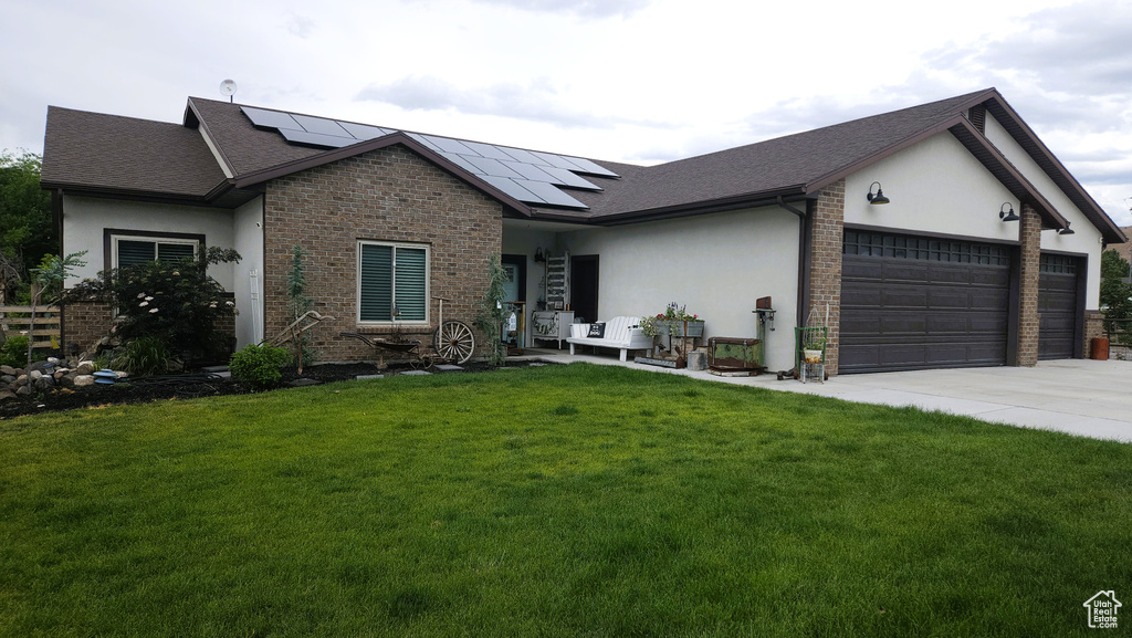 View of front of property featuring a garage, a front lawn, stucco siding, solar panels, and driveway