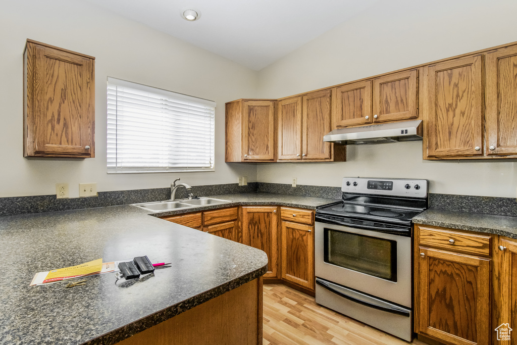 Kitchen featuring under cabinet range hood, stainless steel range with electric cooktop, a sink, and dark countertops