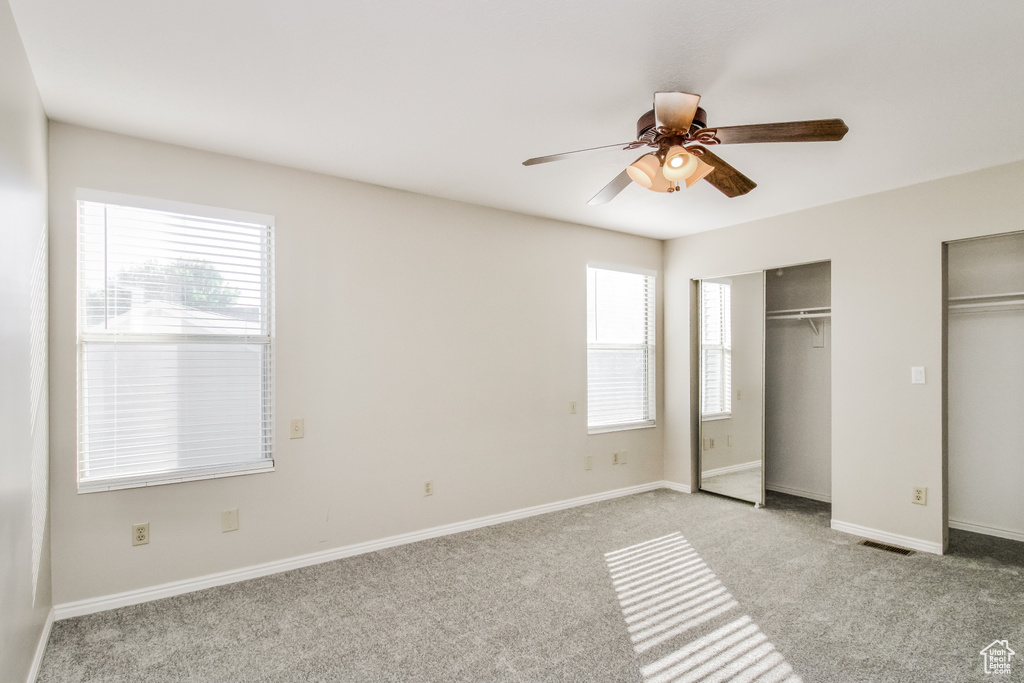 Unfurnished bedroom with multiple closets, light carpet, baseboards, and ceiling fan