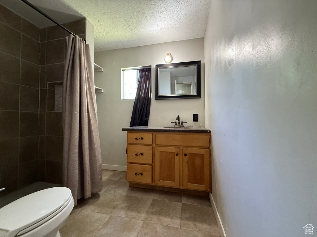 Bathroom featuring vanity, tiled shower, toilet, a textured ceiling, and baseboards